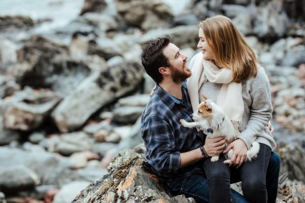 couple sitting on a rocky beach with their dog