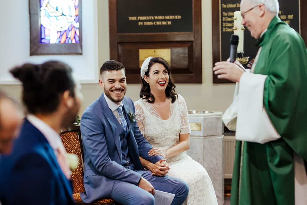 bride and groom laughing with priest during their wedding ceremony